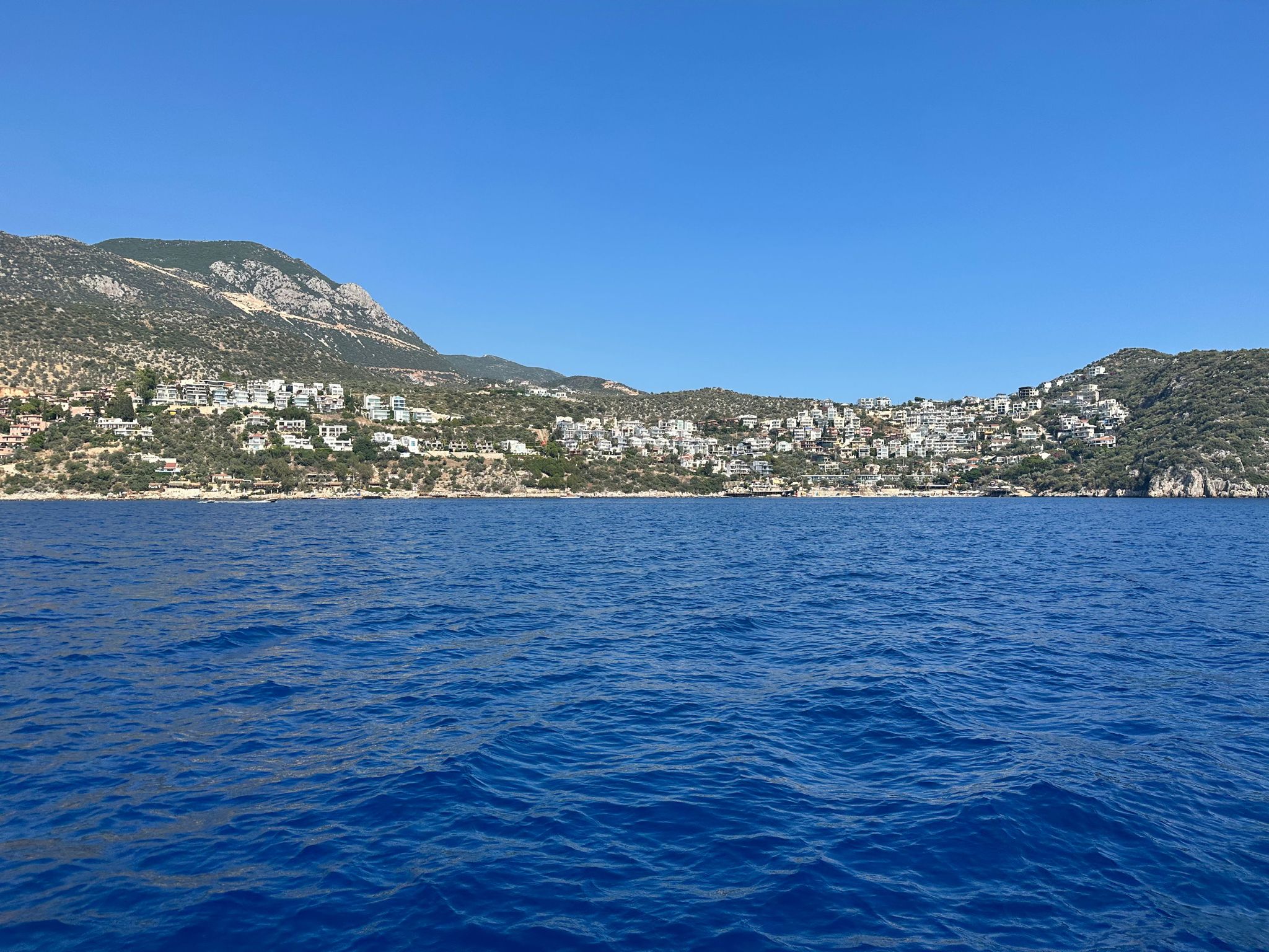 View from the water of the Turkish coastline - deep blue Mediterranean sea with hillside town and mountains under clear skies